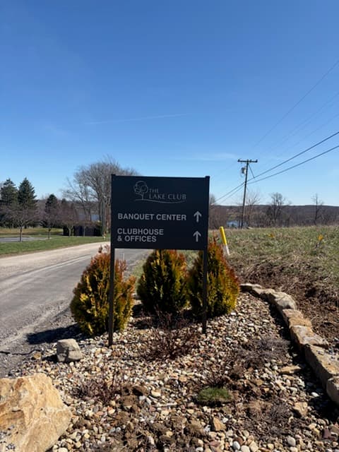Entrance directional sign with banquet center and clubhouse arrows, lake in the distance