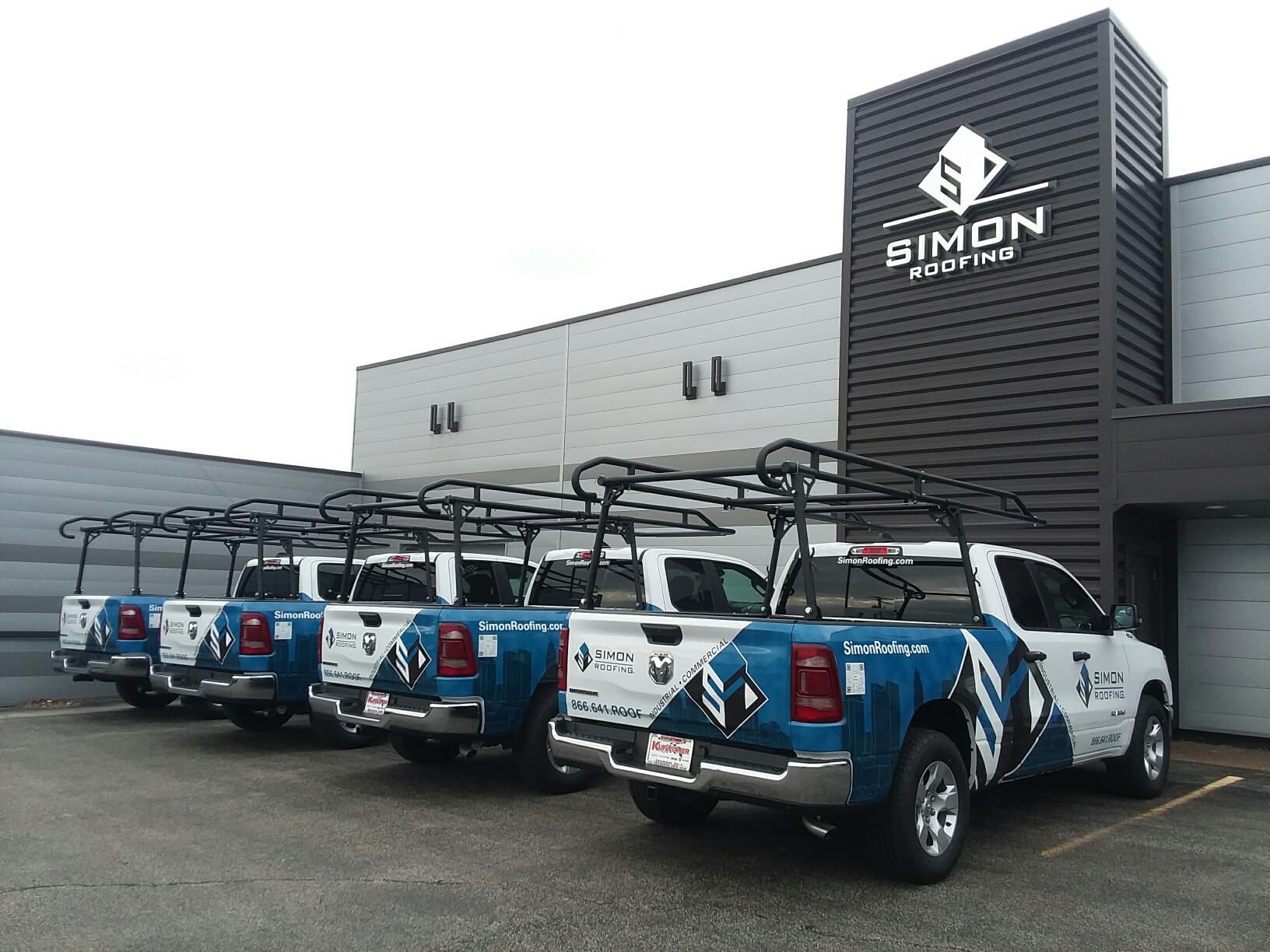 Five Simon Roofing service trucks lined up outside the Simon Roofing facility