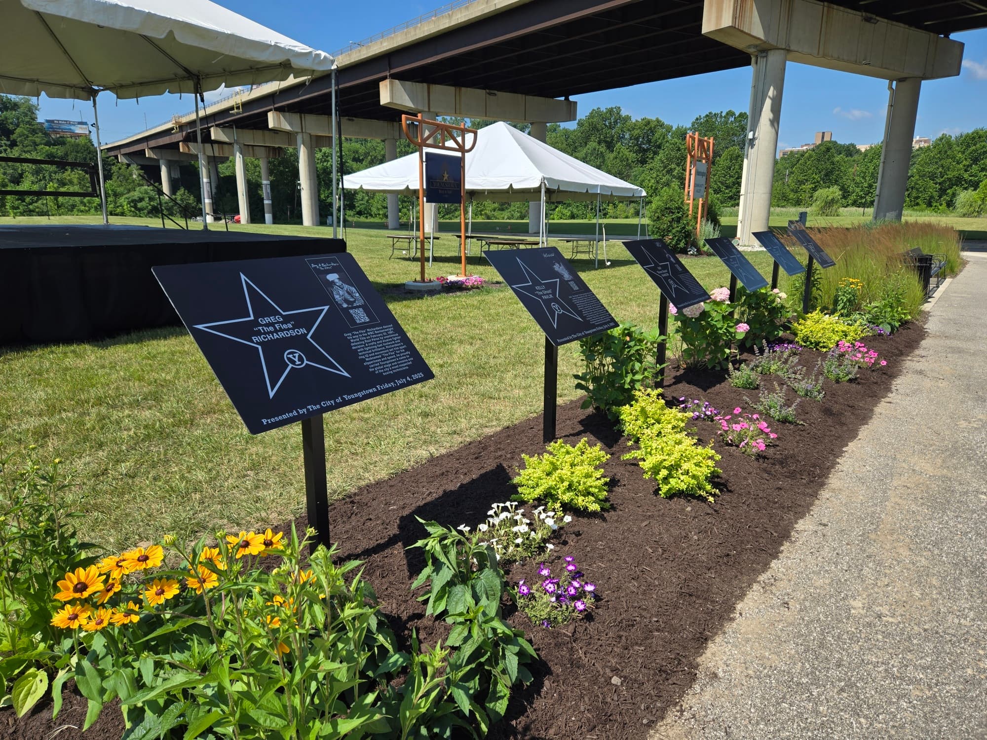 Row of Walk of Fame star plaques in landscaped beds with the Youngstown Walk of Fame truss sign and ceremony tent in the background